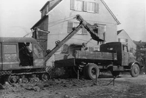 Historische Aufnahme von 1951: Kettenbagger und Lastwagen im Einsatz vor einem Wohnhaus